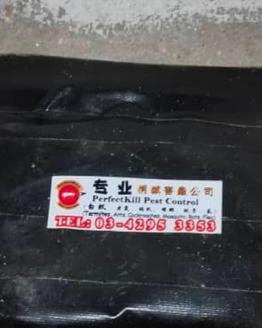 Perfect Kil 的黑色白蚁诱饵站,放在墙边地上,贴着公司印制的标签和办公室电话 03-4295 3353。